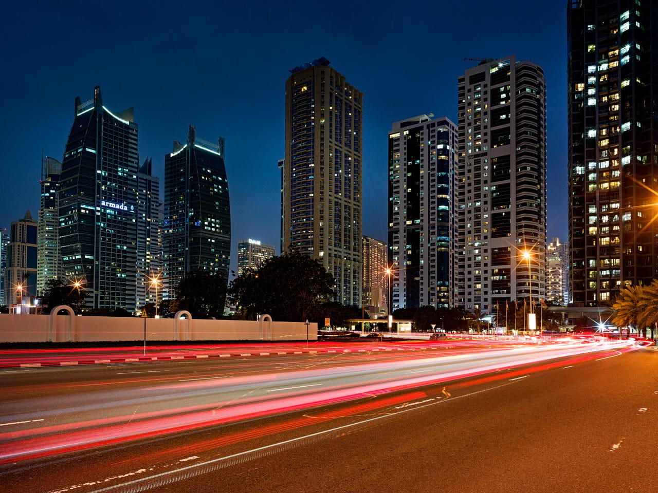 A night-time cityscape featuring tall, modern skyscrapers illuminated against a dark blue sky